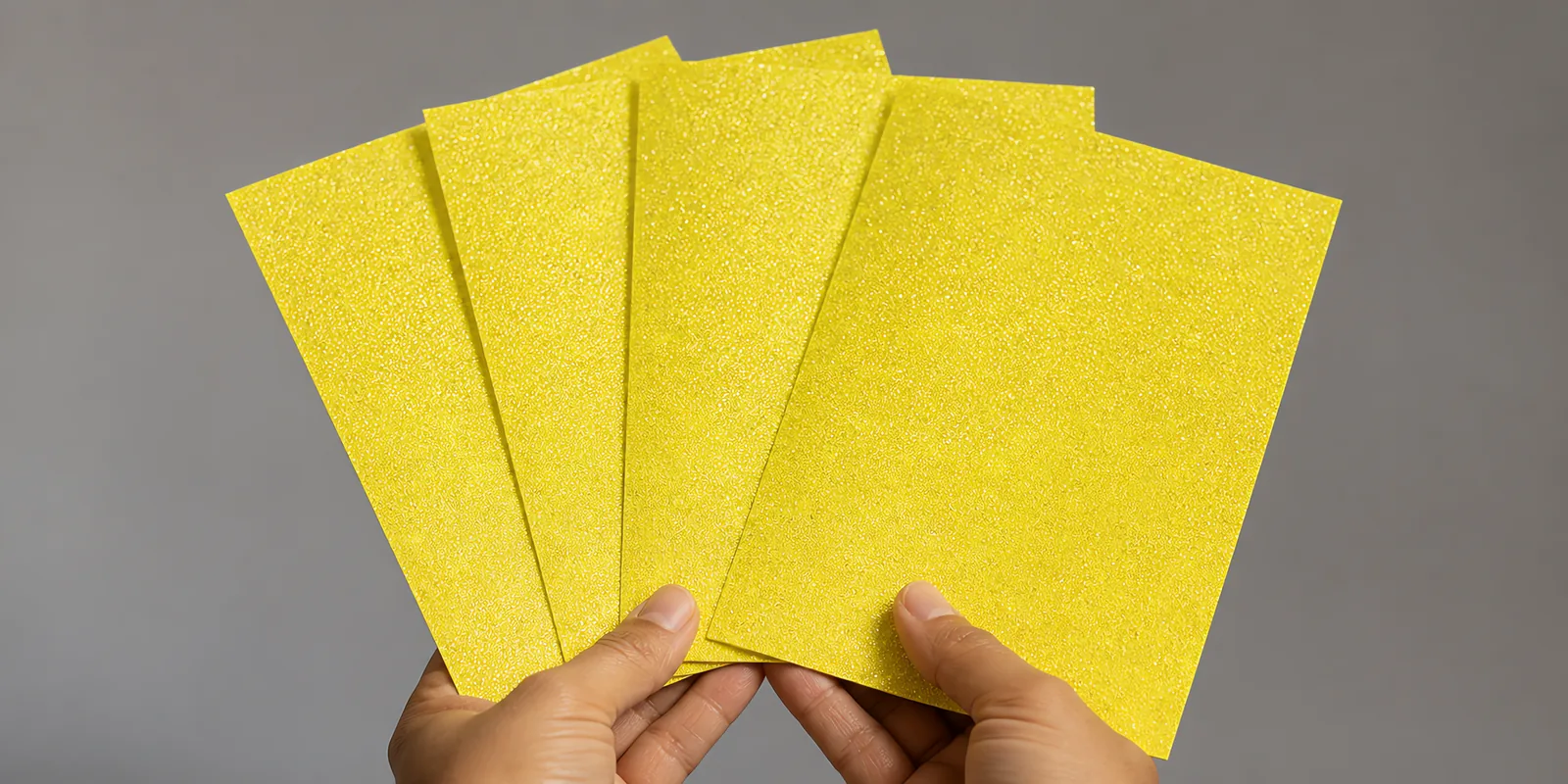 Manos sosteniendo varias hojas de papel con glitter amarillo carruaje brillante abiertas en abanico