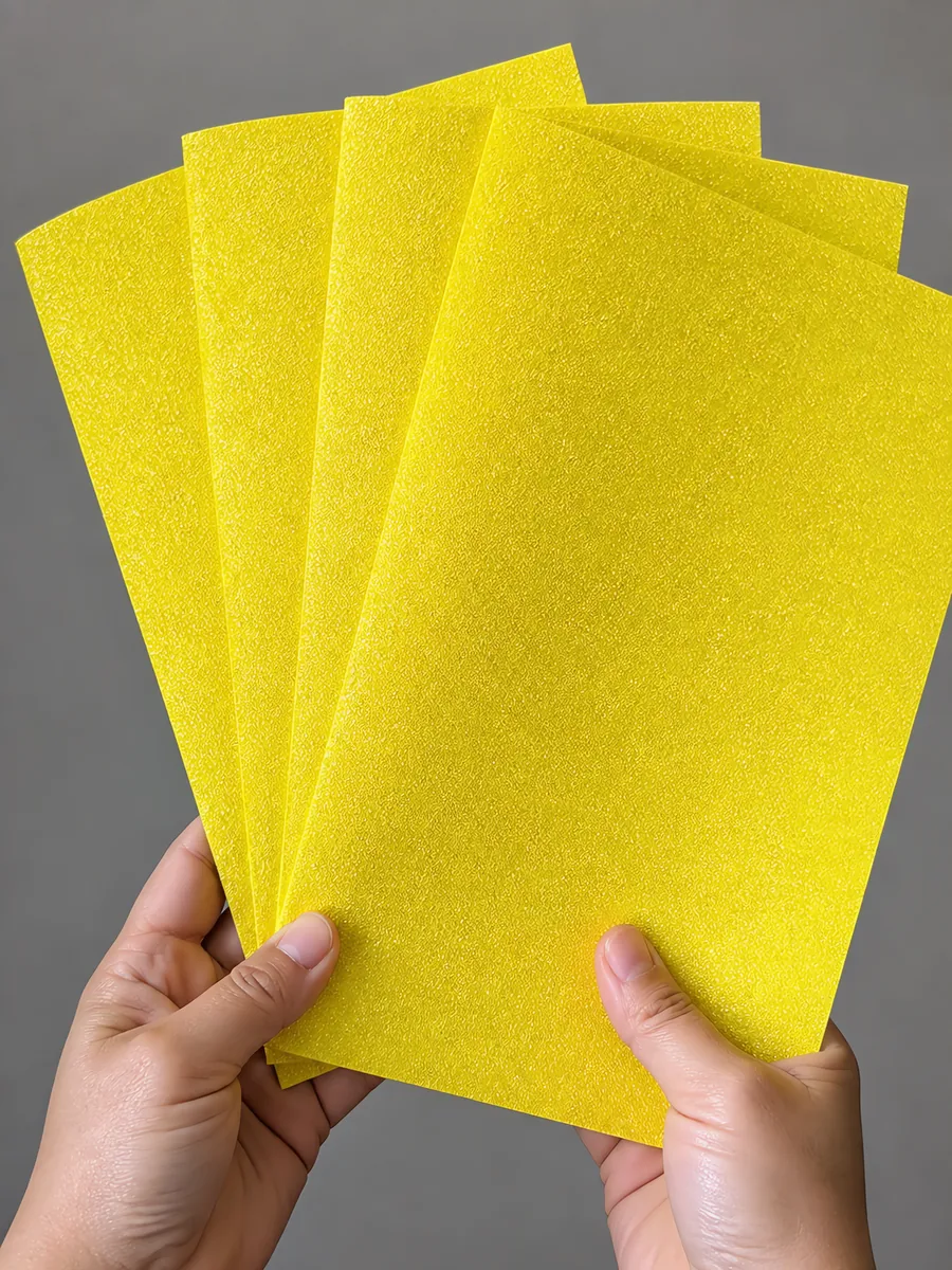 Manos sosteniendo varias hojas de papel con glitter amarillo del tesoro abiertas en abanico