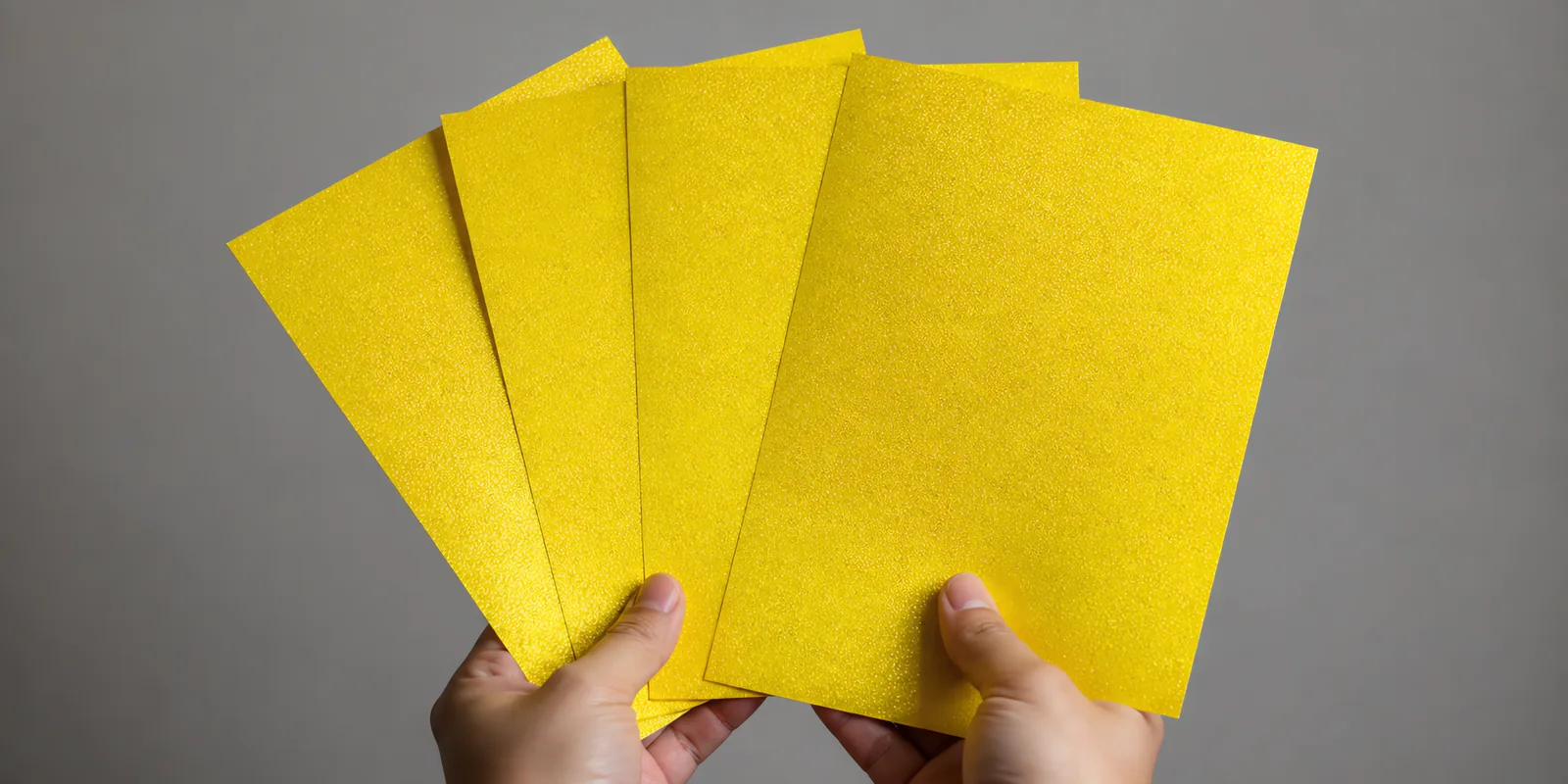 Manos sosteniendo varias hojas de papel con glitter amarillo del tesoro abiertas en abanico
