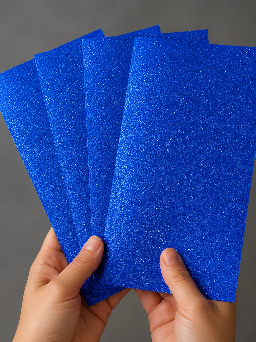 Manos sosteniendo varias hojas de papel con glitter azul castillo luminoso abiertas en abanico