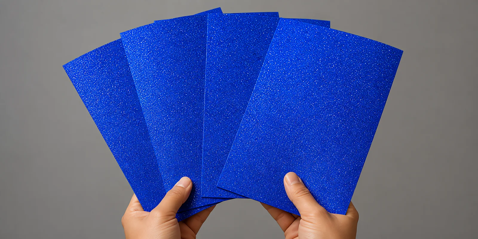 Manos sosteniendo varias hojas de papel con glitter azul castillo luminoso abiertas en abanico