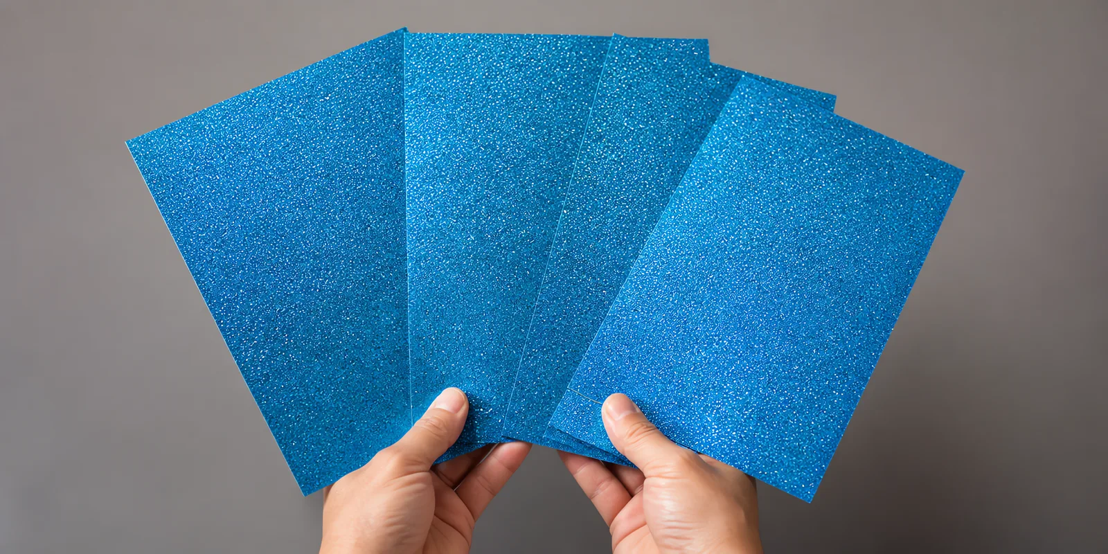 Manos sosteniendo varias hojas de papel con glitter azul gema del dragon abiertas en abanico