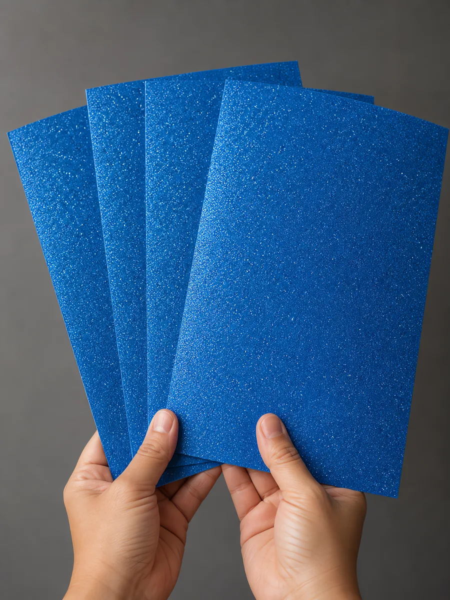Manos sosteniendo varias hojas de papel con glitter azul magia abiertas en abanico