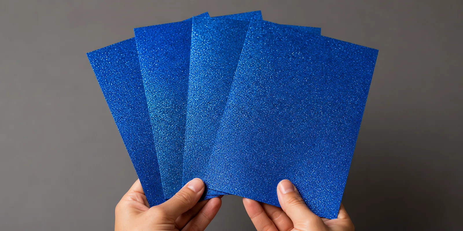 Manos sosteniendo varias hojas de papel con glitter azul magia abiertas en abanico