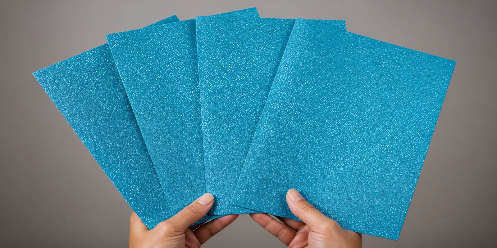 Manos sosteniendo varias hojas de papel con glitter azul principe encantador abiertas en abanico