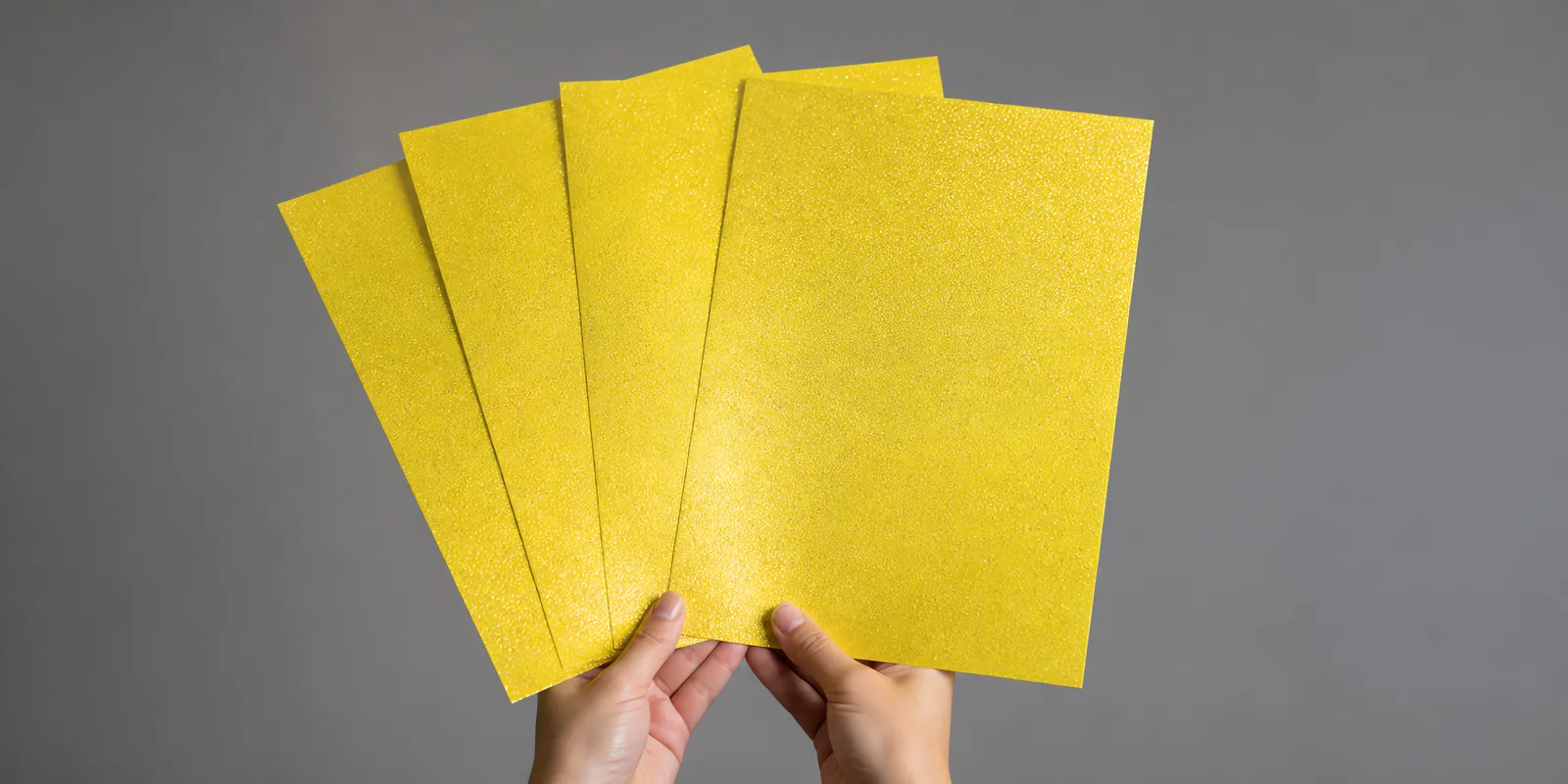 Manos sosteniendo varias hojas de papel con glitter dorado estrella abiertas en abanico