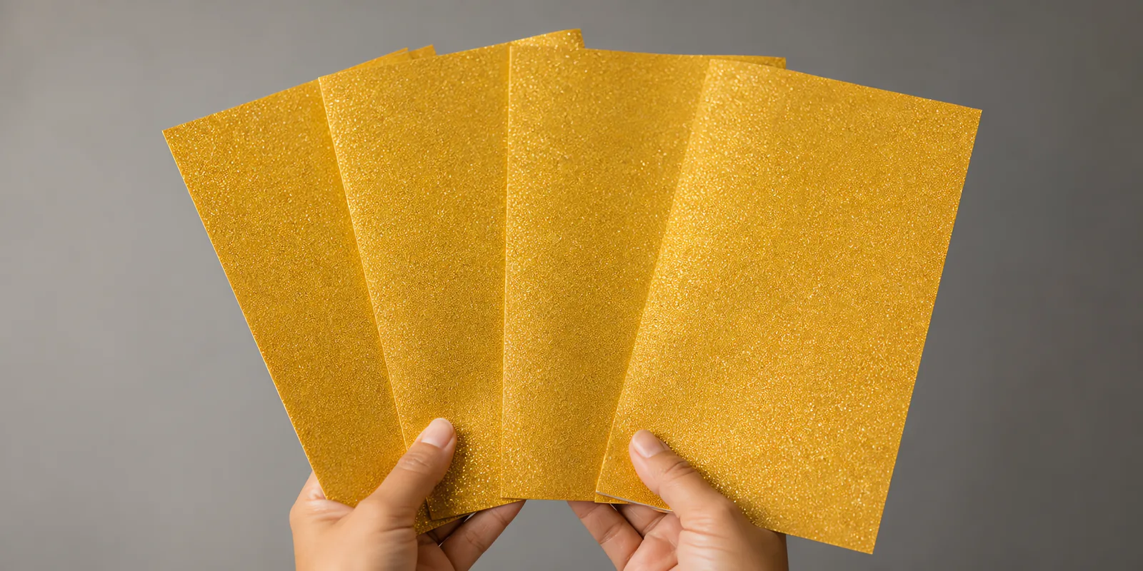 Manos sosteniendo varias hojas de papel con glitter naranja del amanecer abiertas en abanico