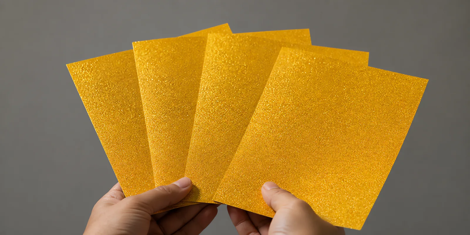 Manos sosteniendo varias hojas de papel con glitter oro anillo encantad abiertas en abanico