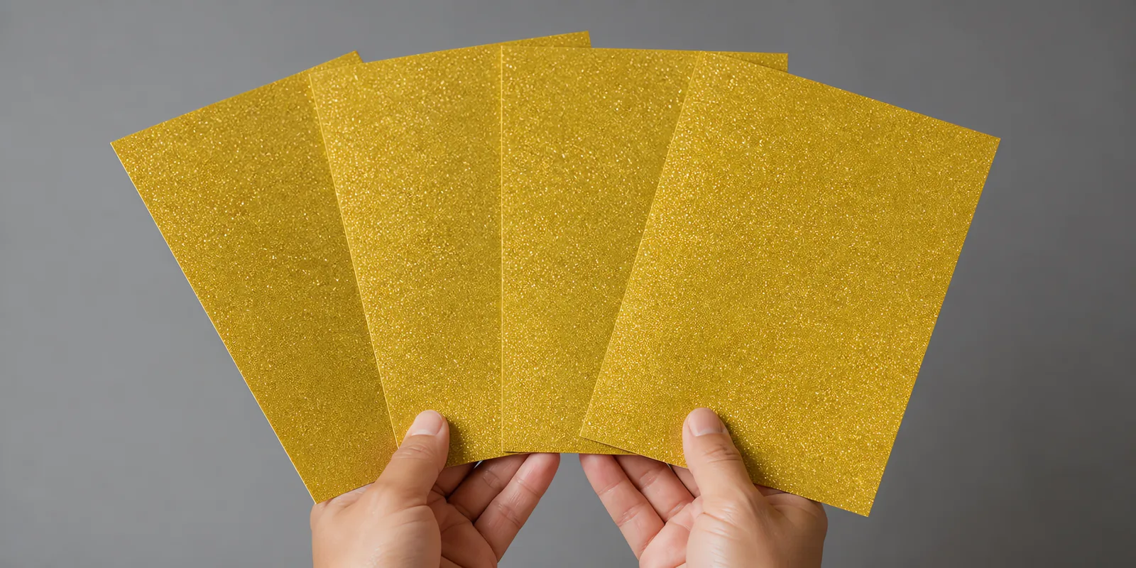 Manos sosteniendo varias hojas de papel con glitter oro corona real abiertas en abanico