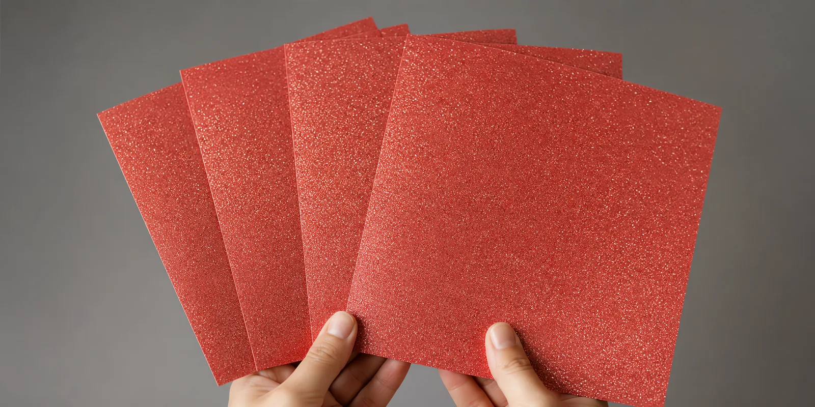 Manos sosteniendo varias hojas de papel con glitter rojo fenix abiertas en abanico