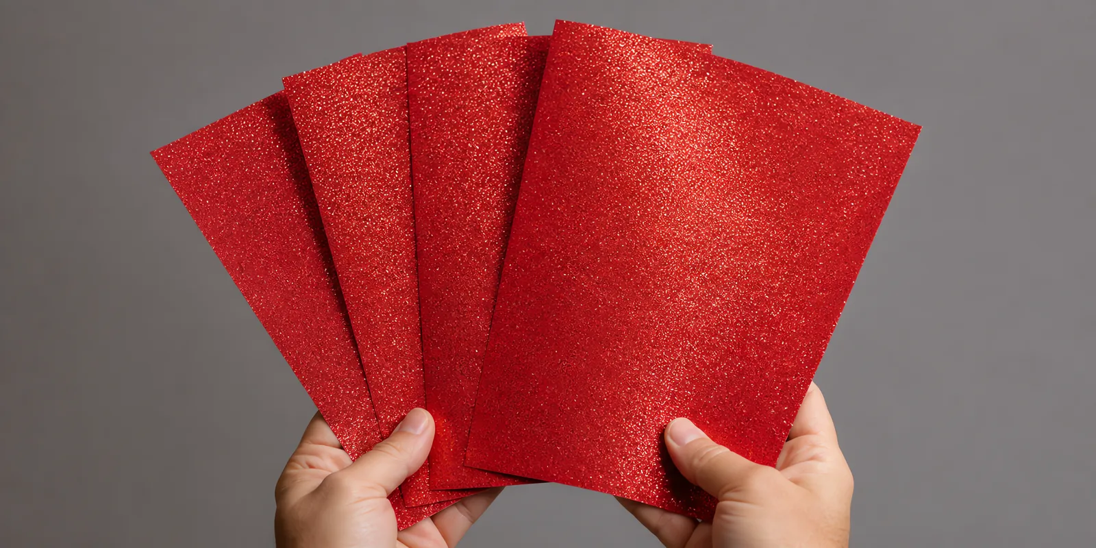 Manos sosteniendo varias hojas de papel con glitter rojo manzana encantada abiertas en abanico