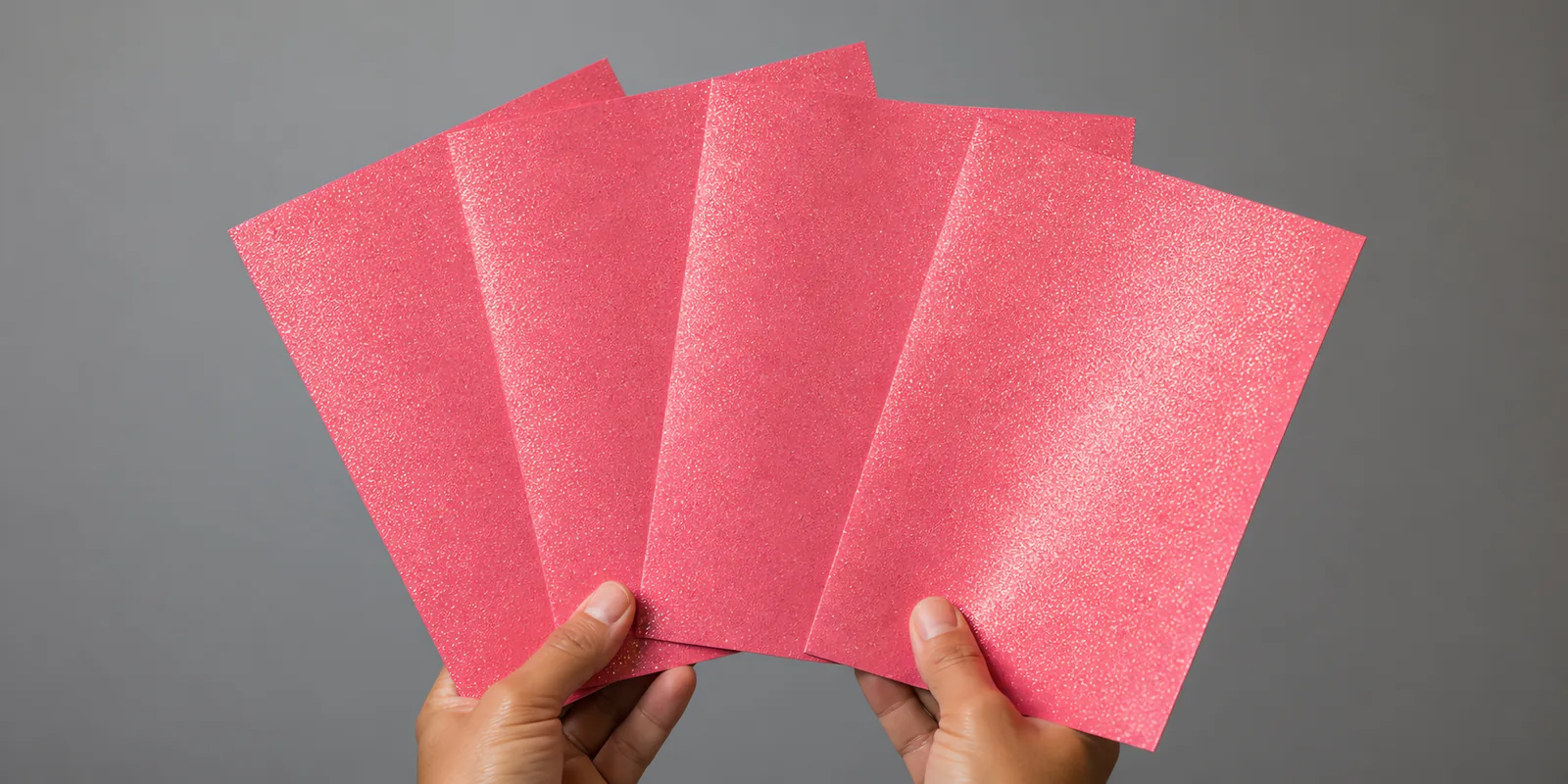 Manos sosteniendo varias hojas de papel con glitter rosa neon magico abiertas en abanico