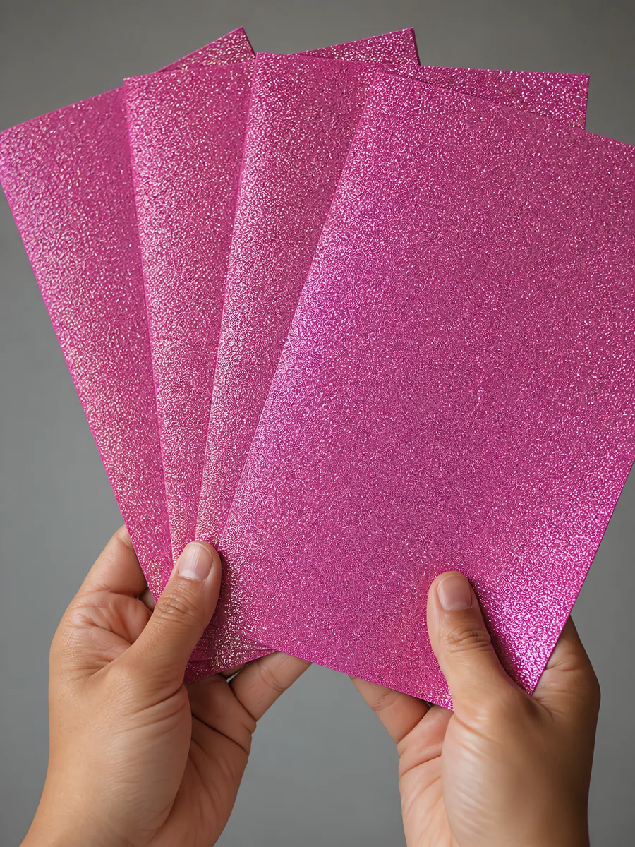 Manos sosteniendo varias hojas de papel con glitter violeta orbe de cristal abiertas en abanico