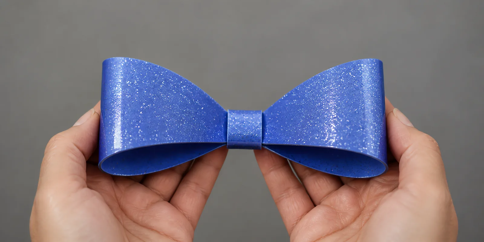 Manos sosteniendo un moño de papel azul con glitter