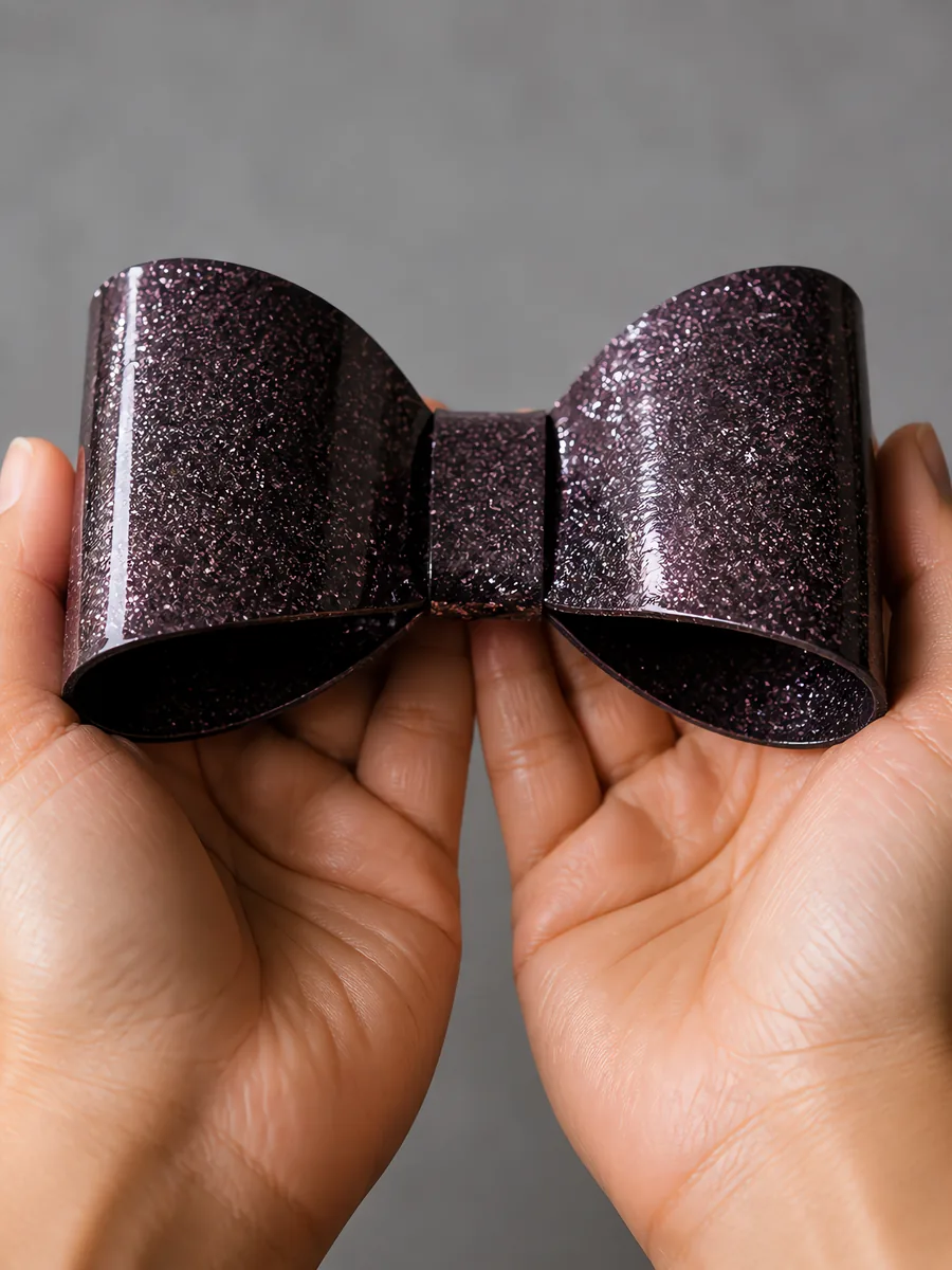 Manos sosteniendo un moño de papel negro brillante con glitter