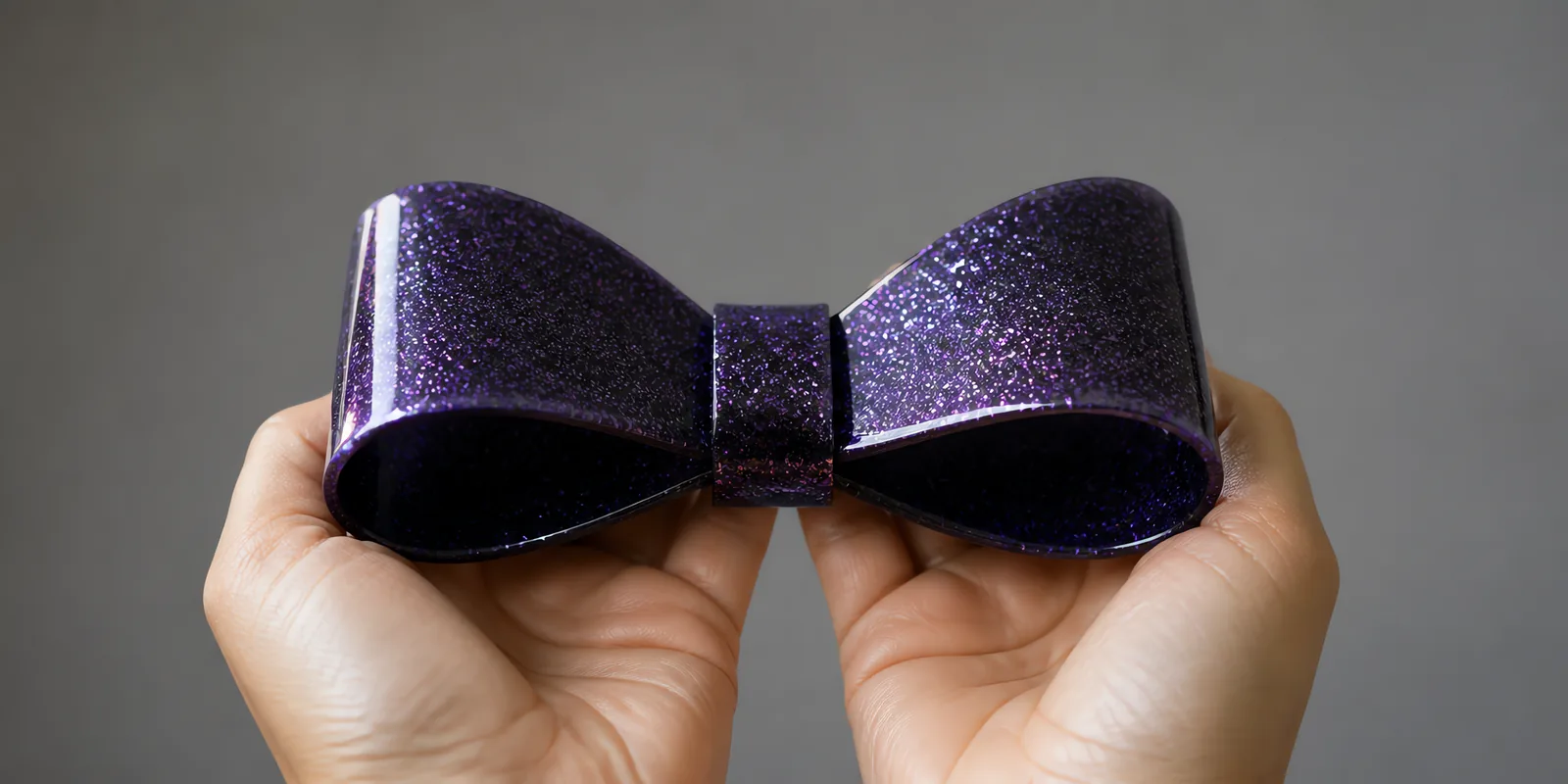 Manos sosteniendo un moño de papel negro brillante con glitter