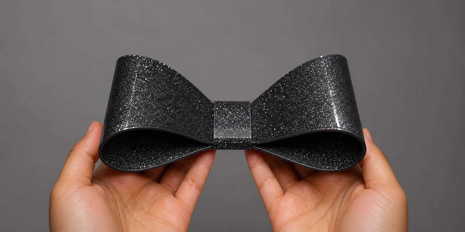 Manos sosteniendo un moño de papel negro noche con glitter