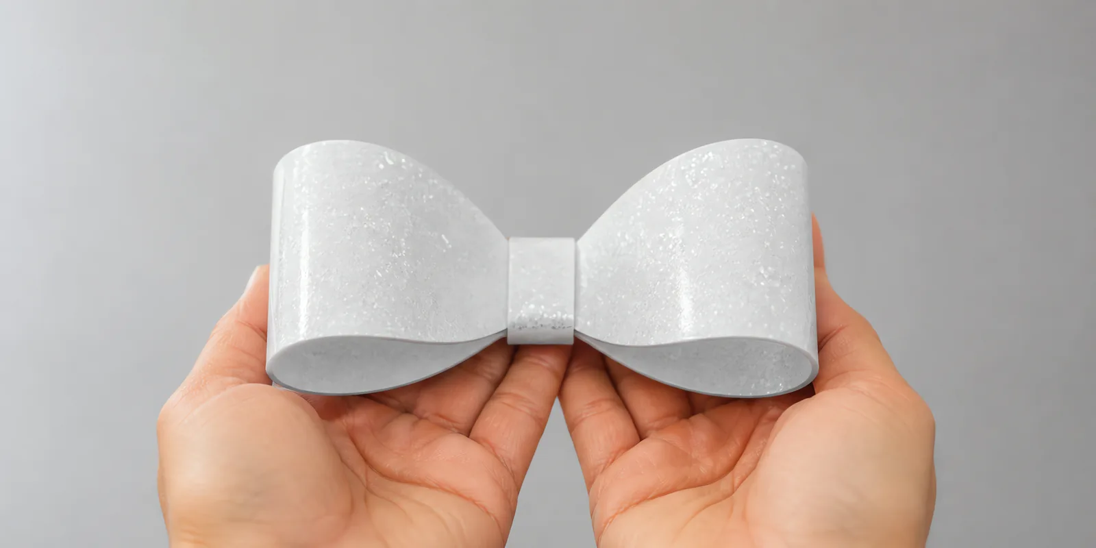 Manos sosteniendo un moño de papel plata espejo con glitter