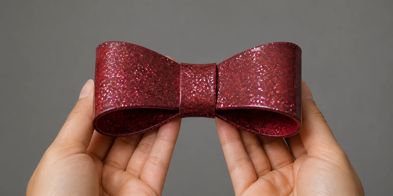 Manos sosteniendo un moño de papel rojo granate con glitter