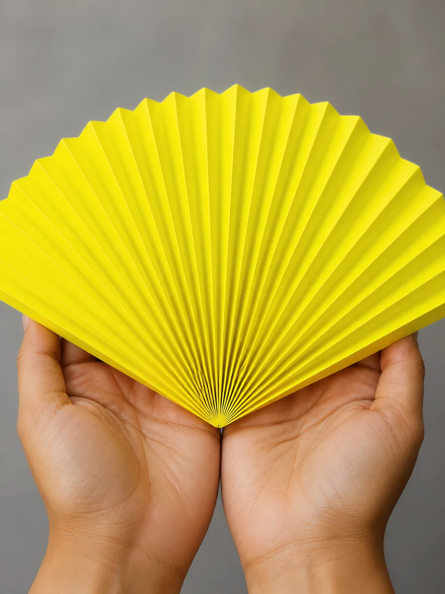 Manos sosteniendo un abanico de papel plegado en acordeón, en amarillo fluor