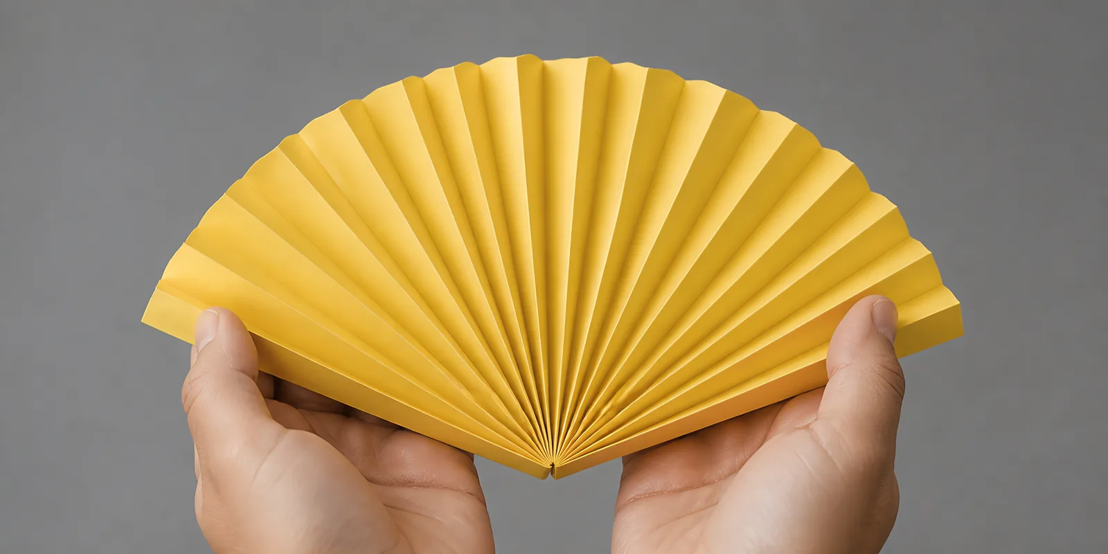 Manos sosteniendo un abanico de papel plegado en acordeón, en amarillo girasol