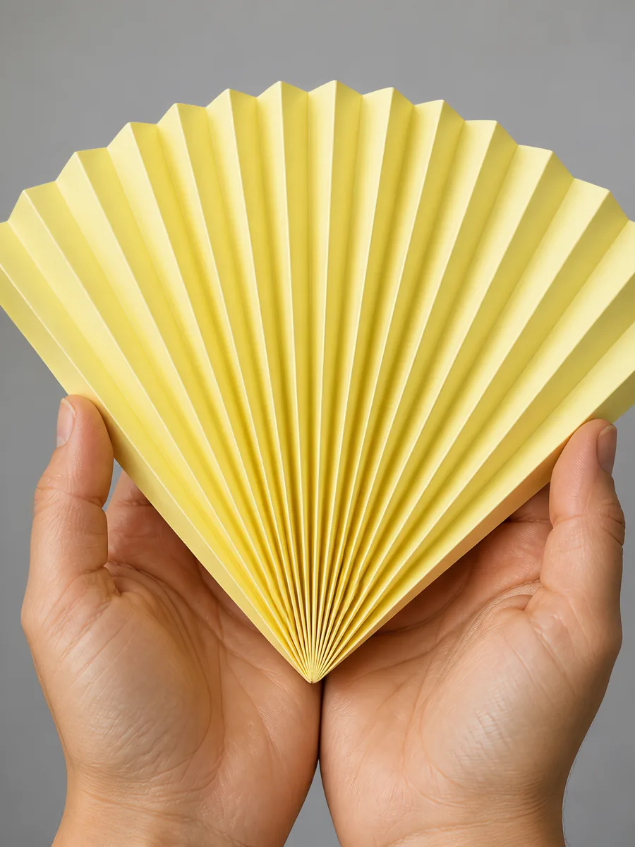 Manos sosteniendo un abanico de papel plegado en acordeón, en amarillo pastel