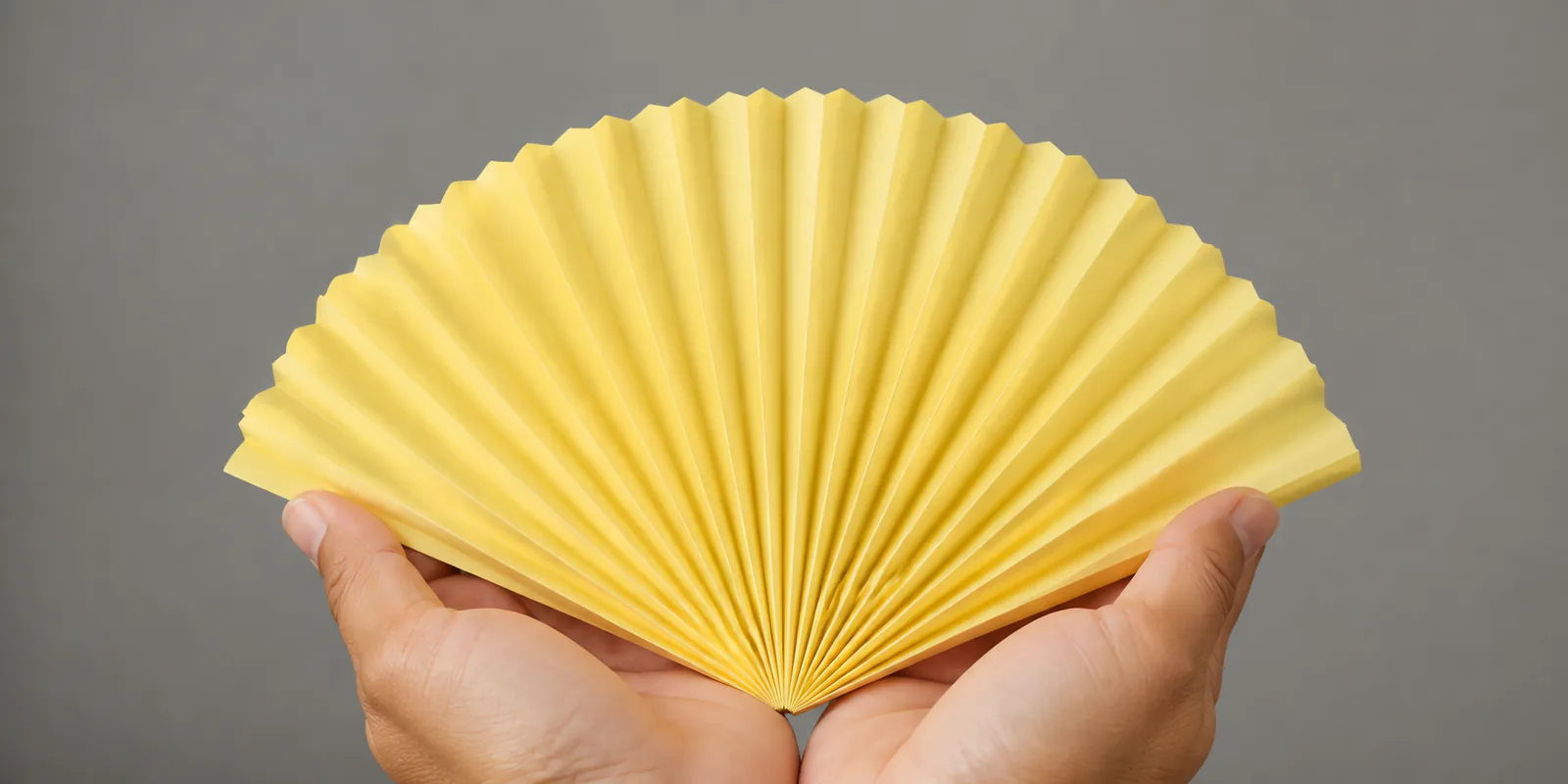 Manos sosteniendo un abanico de papel plegado en acordeón, en amarillo pastel