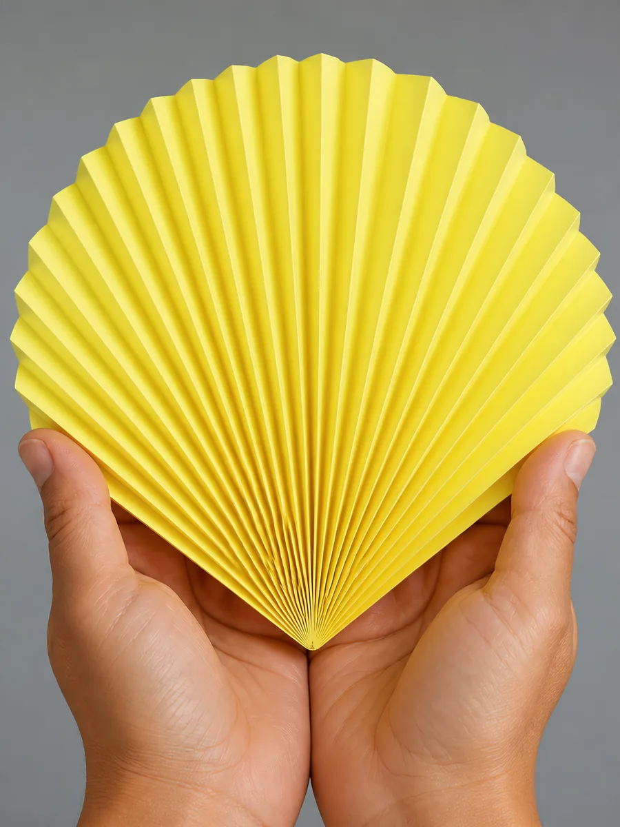 Manos sosteniendo un abanico de papel plegado en acordeón, en amarillo patito