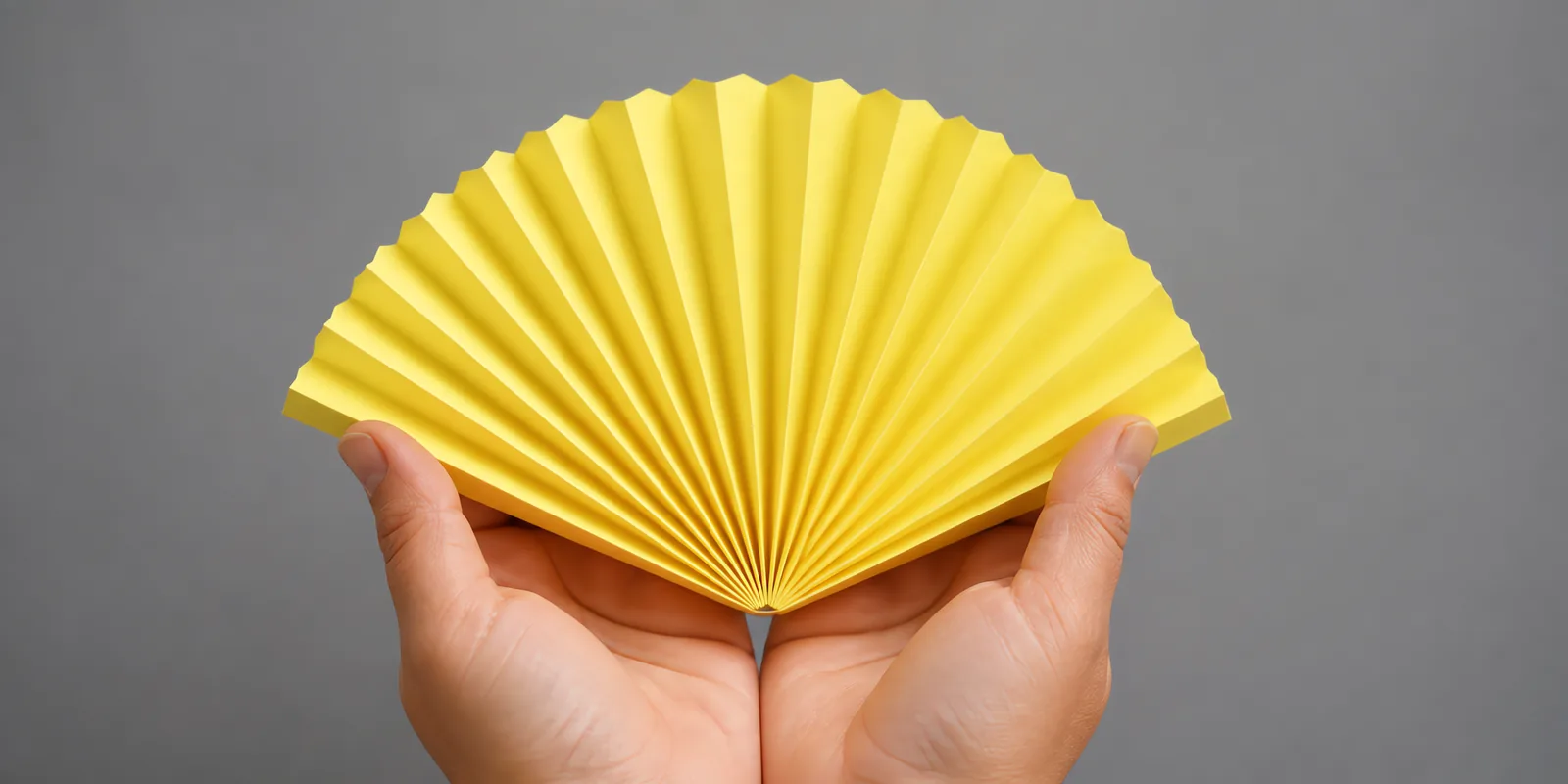 Manos sosteniendo un abanico de papel plegado en acordeón, en amarillo patito
