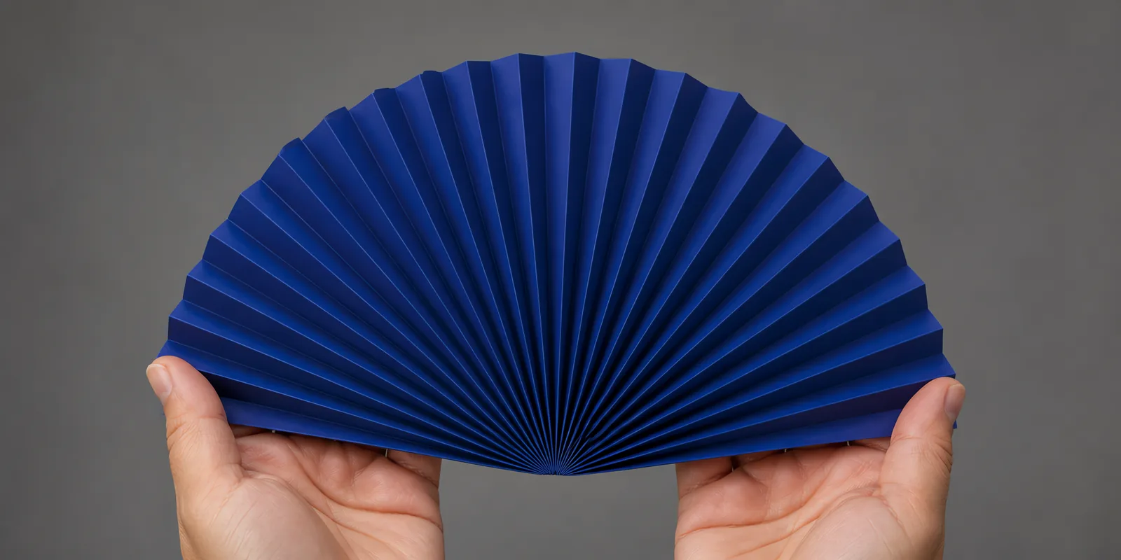 Manos sosteniendo un abanico de papel plegado en acordeón, en azul profundo