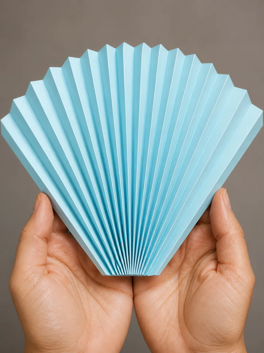 Manos sosteniendo un abanico de papel plegado en acordeón, en celeste pastel