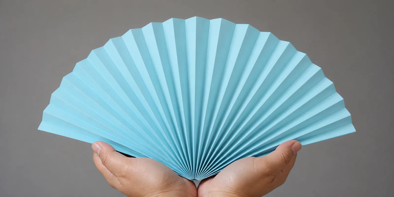 Manos sosteniendo un abanico de papel plegado en acordeón, en celeste pastel
