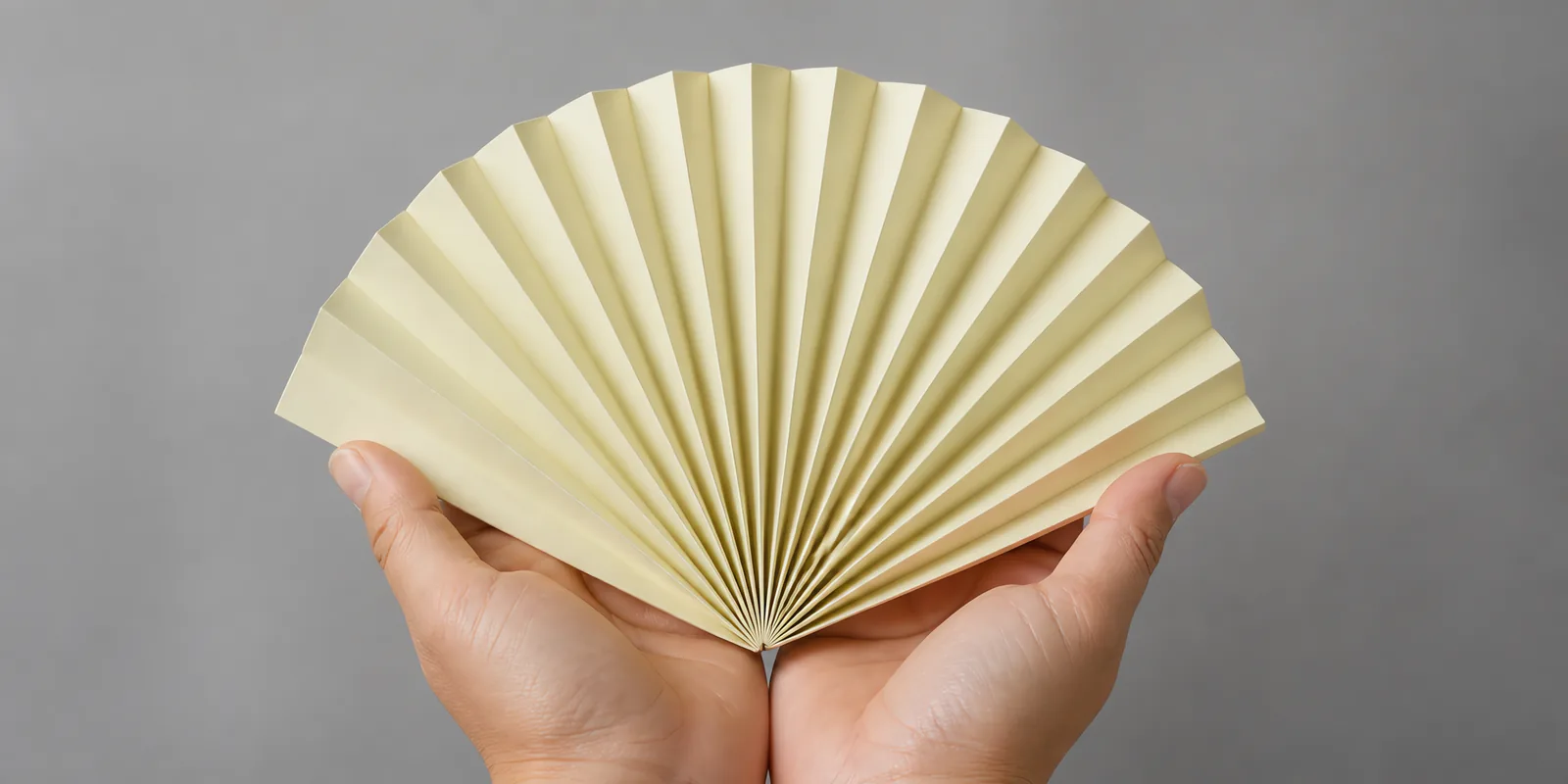 Manos sosteniendo un abanico de papel plegado en acordeón, en crema marfil