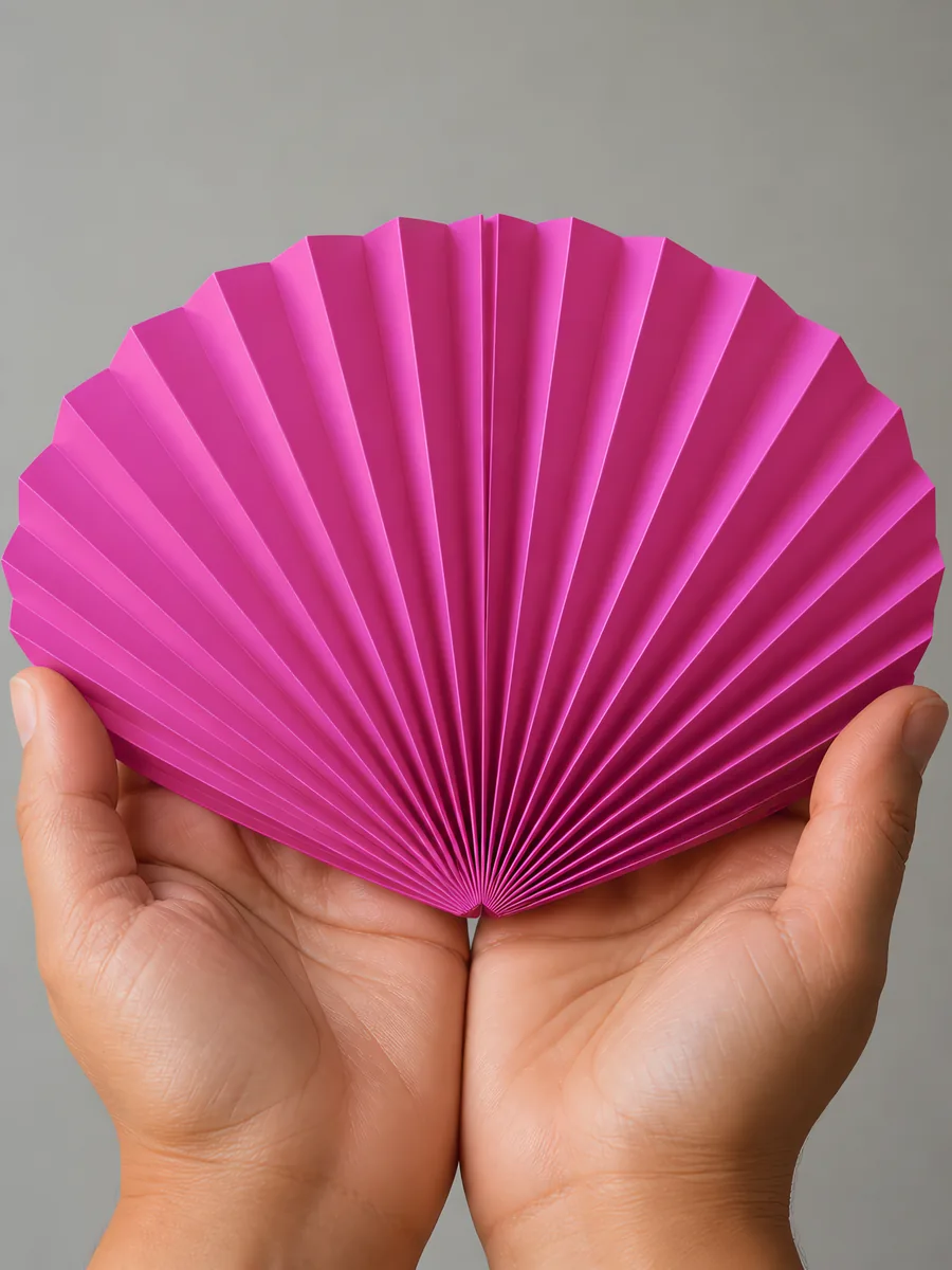 Manos sosteniendo un abanico de papel plegado en acordeón, en fucsia fluor
