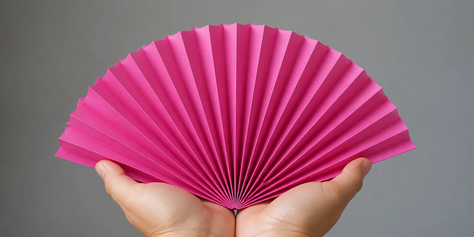 Manos sosteniendo un abanico de papel plegado en acordeón, en fucsia fluor