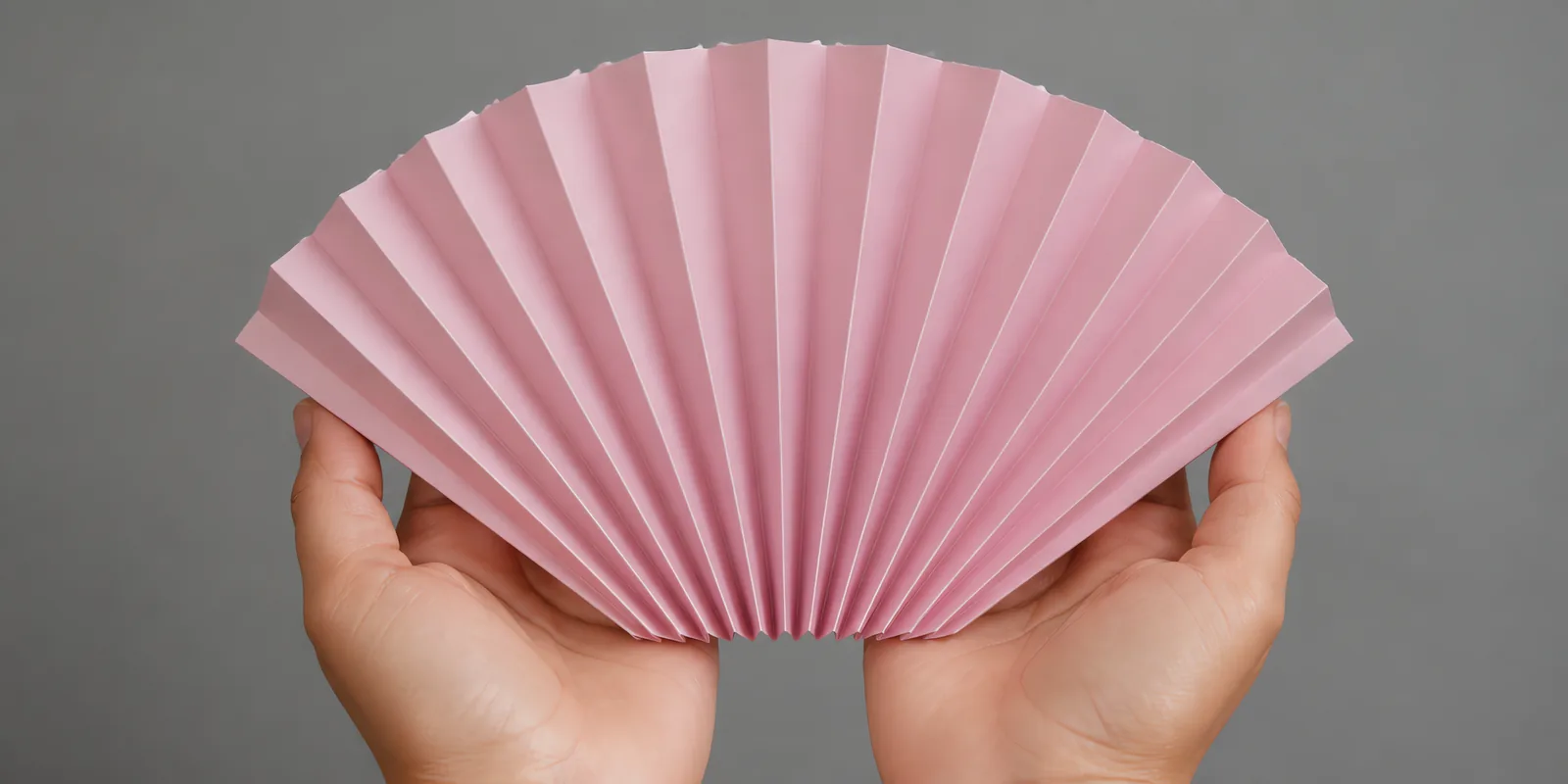 Manos sosteniendo un abanico de papel plegado en acordeón, en rosa rubor
