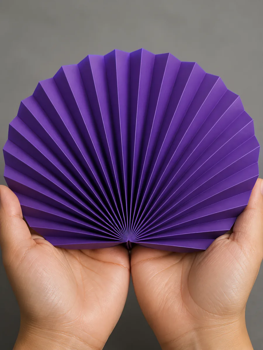 Manos sosteniendo un abanico de papel plegado en acordeón, en ultra violeta