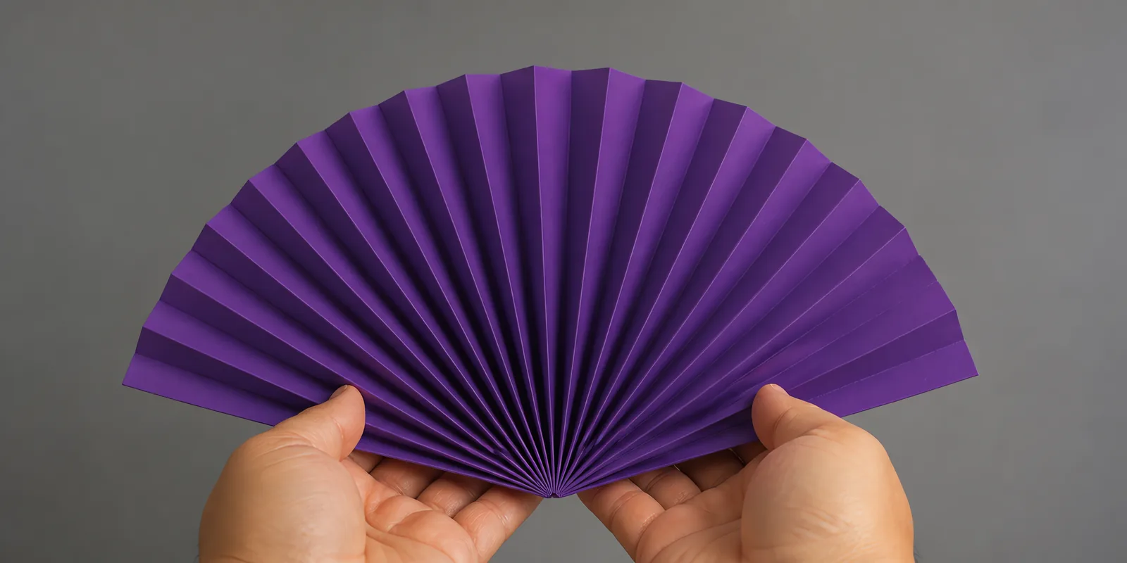 Manos sosteniendo un abanico de papel plegado en acordeón, en ultra violeta