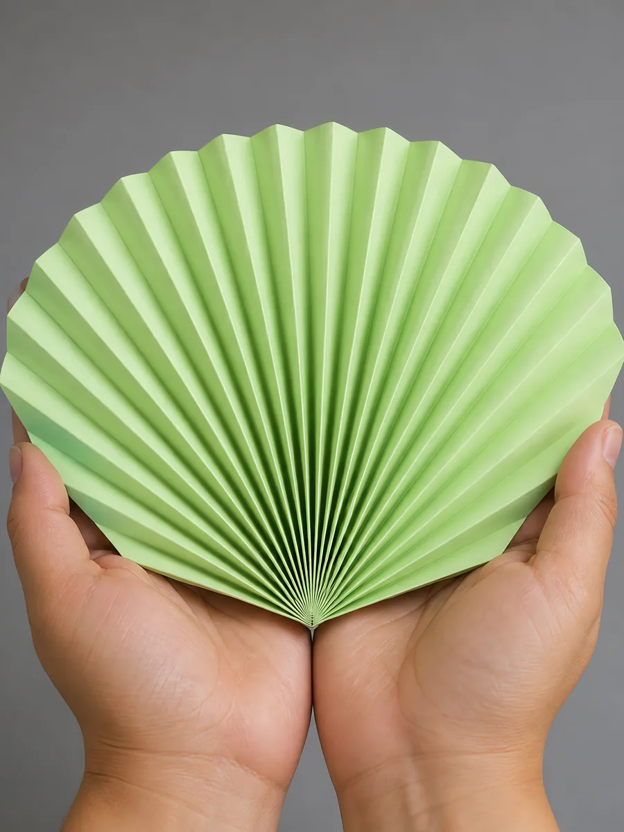 Manos sosteniendo un abanico de papel plegado en acordeón, en verde fluo
