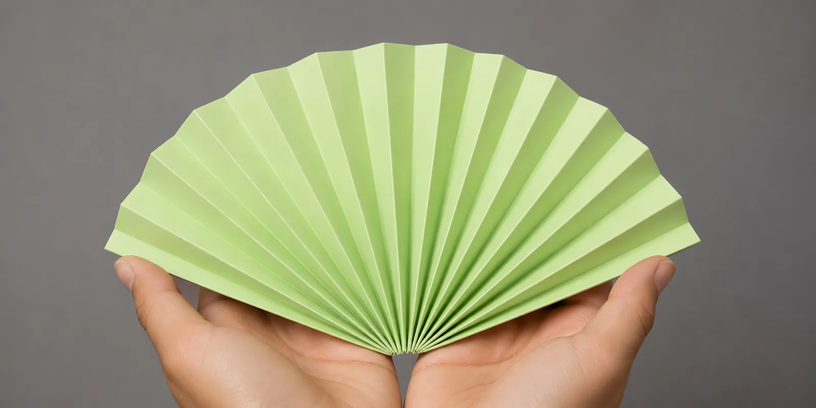Manos sosteniendo un abanico de papel plegado en acordeón, en verde fluo