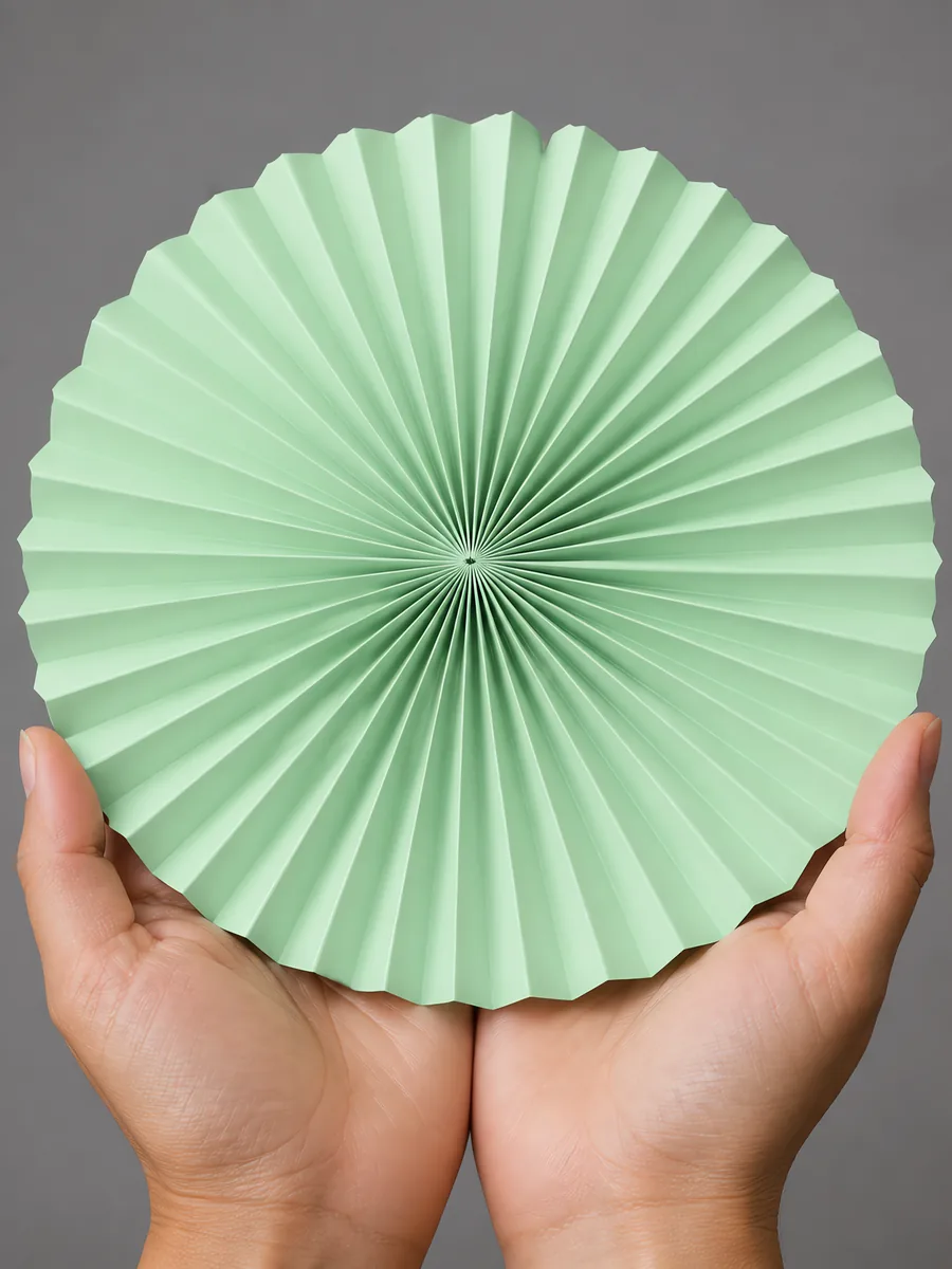 Manos sosteniendo un abanico de papel plegado en acordeón, en verde pastel