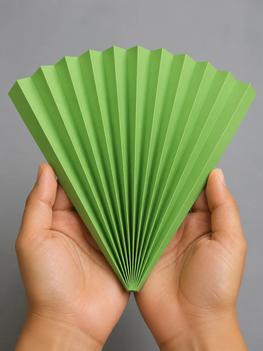 Manos sosteniendo un abanico de papel plegado en acordeón, en verde primavera