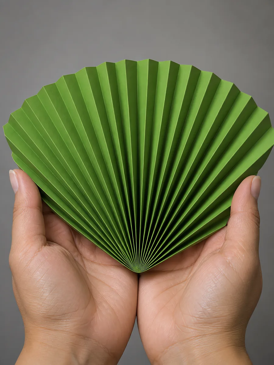 Manos sosteniendo un abanico de papel plegado en acordeón, en verde selva