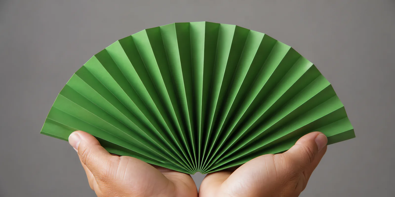Manos sosteniendo un abanico de papel plegado en acordeón, en verde selva