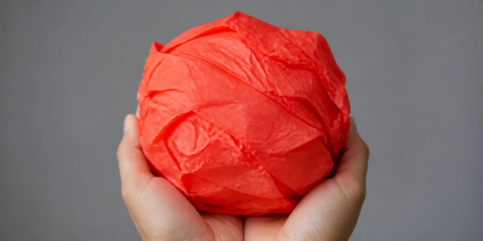 Manos sosteniendo desde abajo un envoltorio de papel seda coral fluor
