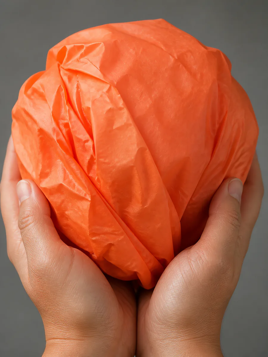 Manos sosteniendo desde abajo un envoltorio de papel seda naranja fluor