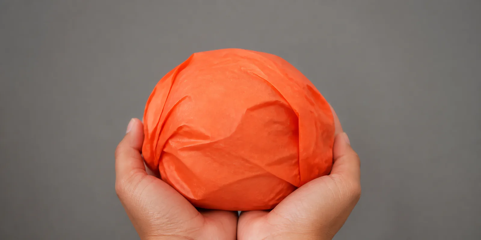 Manos sosteniendo desde abajo un envoltorio de papel seda naranja fluor