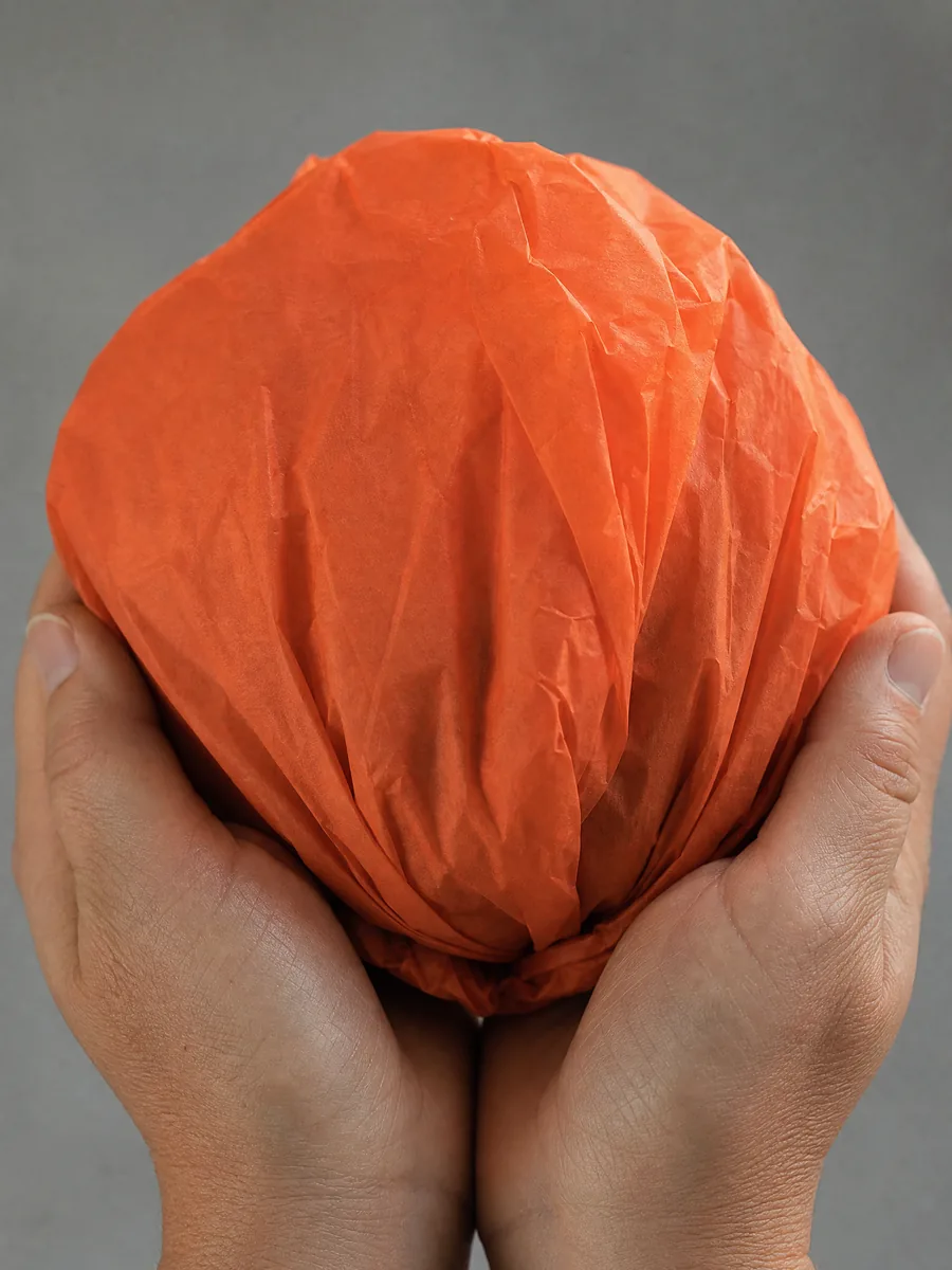 Manos sosteniendo desde abajo un envoltorio de papel seda naranja