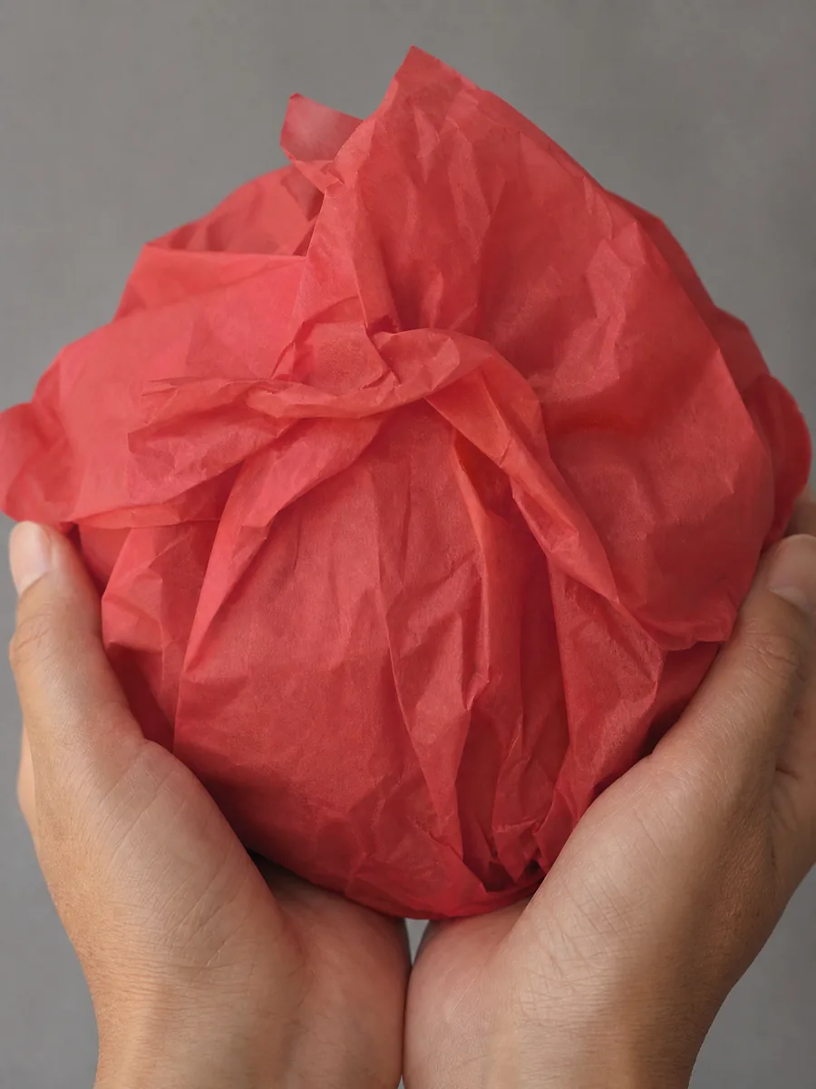 Manos sosteniendo desde abajo un envoltorio de papel seda rojo carmesi