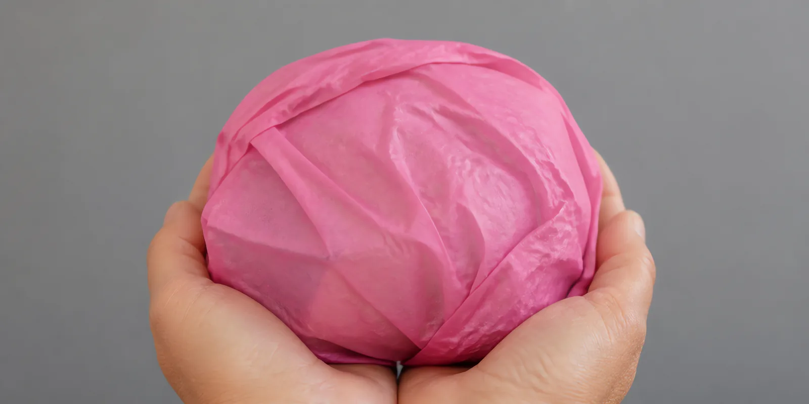 Manos sosteniendo desde abajo un envoltorio de papel seda rosa chicle